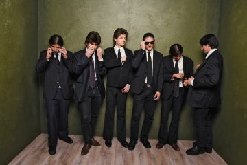 Sechs Männer mit schwarzen Anzügen, Krawatten und Sonnenbrillen bilden das Wolfpack